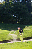 Golfer hitting out of bunker, Prien am Chiemsee, Bavaria, Germany