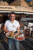 Waiter serving Greek food in a restaurant at harbor, Chania, Chania Prefecture, Crete, Greece