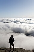 A hiker takes in the view of undercast from the summit of Mount Osceola in the White Mountains, New Hampshire USA