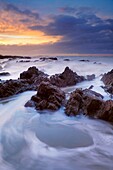 The incoming tide washing over the rocks at dusk at Westward Ho! in Devon, England