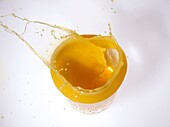 slice of orange splashing into a glass of orange juice from above