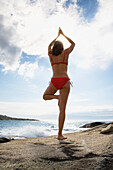 Woman exercising yoga at beach, bay of Algajola, Corsica, France