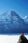 Frau sitzt auf Felsen und blickt auf Nordwand des Eiger über Nebelmeer, Bussalp, Grindelwald, UNESCO Welterbe Schweizer Alpen Jungfrau - Aletsch, Berner Oberland, Bern, Schweiz, Europa