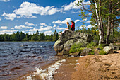 Mother and daughter sitting on a rock at lake Store Hindsjon, Kalmar county, Smaland, Sweden