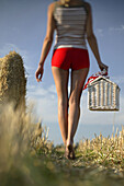 Junge Frau läuft mit einem Picknickkorb durch ein Stoppelfeld, Obberbayern, Deutschland