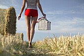 Young woman with picnic basket walking through stubblefield, Upper Bavaria, Germany