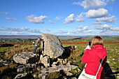Young women taking a photo of boyfriend pushing stone, King Arthurs Stone, Cefn Bryn, Gower peninsula, south-Wales, Wales, Great Britain