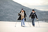 Zwei junge Frauen gehen mit Schneeschuhen über verschneite Wiese, Leitzachtal, Oberbayern, Bayern, Deutschland, Europa