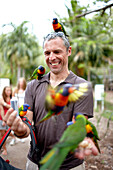 Tourist mit Rainbow Lorikeet Papageien im Bungalow Bay Koala Village, Horseshoe Bay, Nordküste Magnet Island, Great Barrier Reef Marine Park, UNESCO Weltkulturerbe, Queensland, Australien