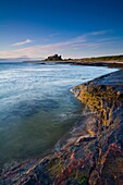 England, Northumberland, Bamburgh Bamburgh Castle, beach and dunes viewed shortly after sunrise from Harkess Rocks