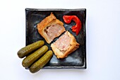 Two wedges of common British pork pie with miniature gherkins and roasted red peppers