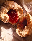 upright close up of a jam donut broken in half with fruit jam pouring out