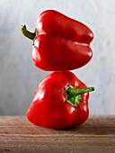 2 red peppers balanced on top of each other against a black background