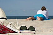 Woman lying at beach, book and sunglasses in foreground, List, Sylt, Schleswig-Holstein, Germany
