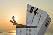 Woman relaxing in roofed wicker beach chair in sunset, Westerland, Sylt, Schleswig-Holstein, Germany