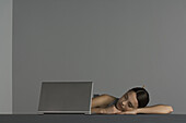 Woman napping next to laptop computer, head resting on arms