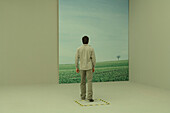 Man stepping toward large photograph of rural scene, hazard tape on the floor around him