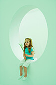 Little girl sitting on windowsill, holding flowers