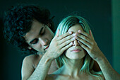 Young couple together, man covering woman's eyes with hands
