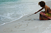 'Woman crouching on beach, writing word ''peace'' in sand with stick'
