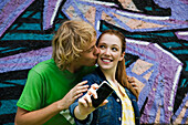 Young couple photographing themselves with cell phone, male kissing female's cheek
