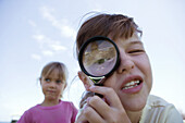 Girl looking through magnifying glass, looking at camera, close-up