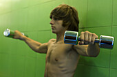 Young man holding dumbbells out to side, side view