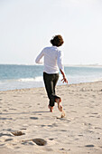 Cape Verde Peninsula, Sal, Santa Maria beach, teenage boy running on the beach, rear view