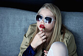 Young Blonde Girl in Sunglasses Putting on Red Lipstick
