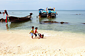 Thai children playing at the beach near long tail boats, Koh Jum, Andaman Sea, Thailand