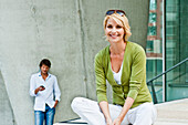 Woman sitting on step, man with mobile phone standing in background, HafenCity, Hamburg, Germany