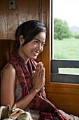 Bildschöne asiatische Frau zelebriert Wai Begrüßung in einem Waggon für Touristen auf der Trans-River Kwai Death Railway Eisenbahn entlang dem Fluss River Kwai Noi, nahe Kanchanaburi, Thailand, Asien
