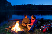 Young couple sitting at a campfire in the evening, lake Ottenstein, Lower Austria, Austria, Europe