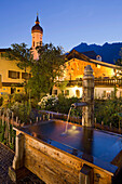 Brunnen und beleuchtete Häuser in der Abendämmerung, Garmisch Partenkirchen, Bayern, Deutschland, Europa