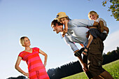 Father giving children piggyback ride, woman smiling, Lake Starnberg, Bavaria, Germany