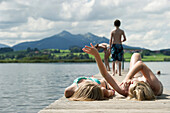 Two teenage girls sunbathing on a jetty at lake Hopfensee, Fuessen, Allgaeu, Bavaria, Germany