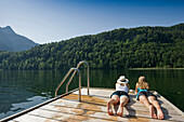 Two teenage girls lying on a jetty at lake Schwansee, Schwangau, Allgaeu, Bavaria, Germany