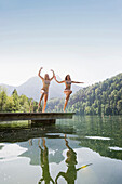 Two girls jumping into lake Schwansee, Schwangau, Allgaeu, Bavaria, Germany