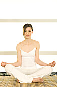 Young woman sitting cross-legged, yoga attitude, looking at the camera