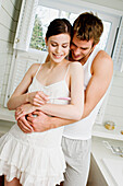 Smiling couple embracing in bathroom, looking at pregnancy test