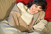 Young woman lying on a sofa, smiling, wrapped in blanket