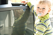 Little boy with pacifier taking TV remote control