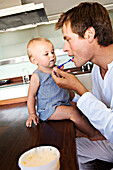 Father and baby in kitchen, man feeding his son, indoors