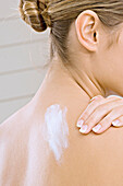 Rückansicht einer jungen Frau, die sich die Schulter mit Feuchtigkeitscreme eincremt