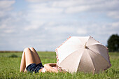 Young woman lying in grass, behind an umbrella