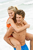 Man giving woman piggyback ride on the beach