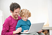 Close-up of a man assisting his son in using a laptop