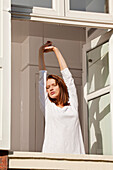 Young woman stretching at window