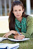 Portrait of young woman lying on grass and studying in a campus