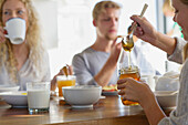 Family eating breakfast at home with focus on a girl taking out honey